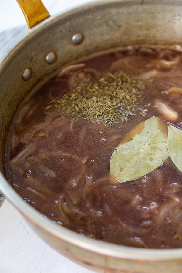A copper pan with broth and onions and bay leaves.