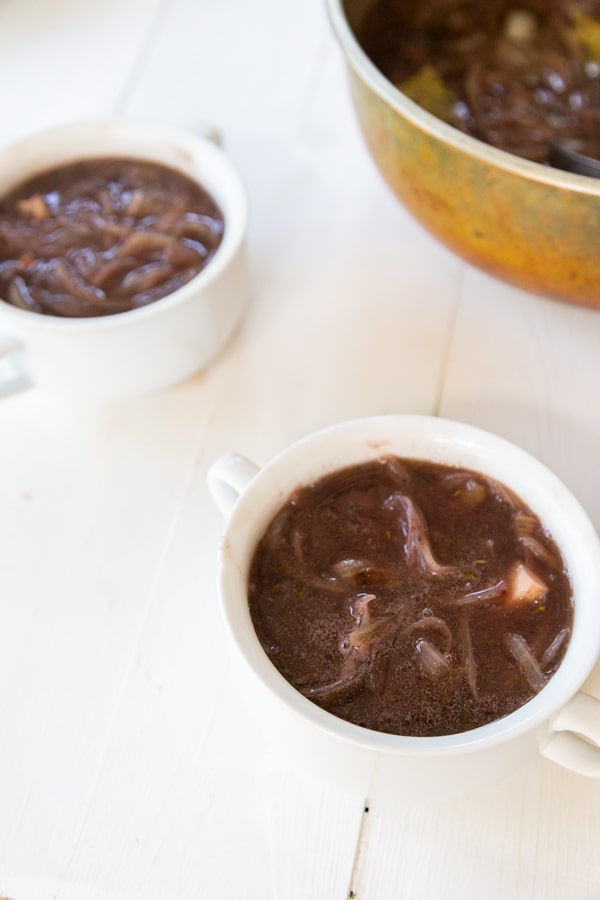 Two white bowls with onion soup and a copper pot with the soup.