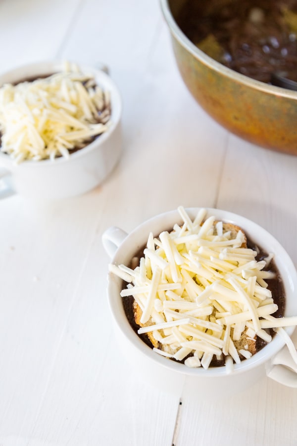Two white bowls with onion soup, a slice of bread, and shredded mozzarella cheese.