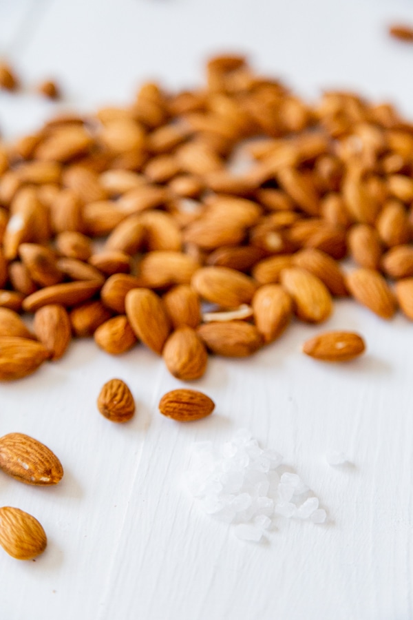 A pile of almonds and sea salt on a white wood surface. 