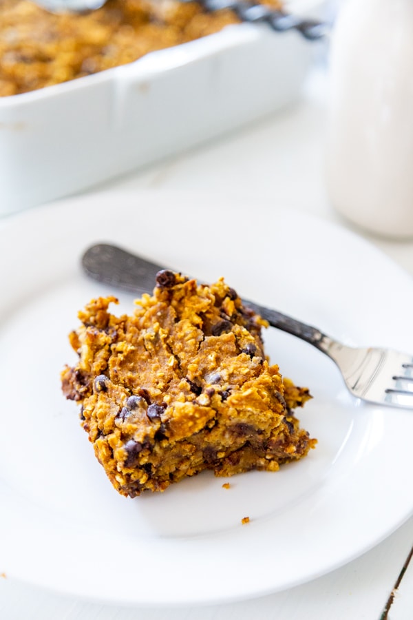 A slice of pumpkin blondie on a white plate with a fork on the rim of the plate.