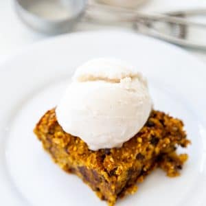 A chocolate chip blondie on a white plate with a scoop of ice cream on top.