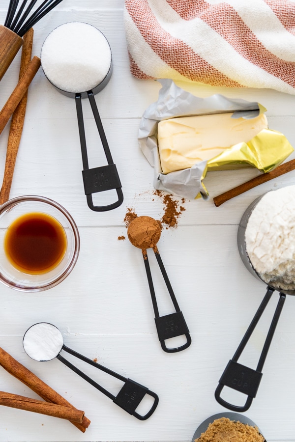 A white wood table with black measuring cups and spoons filled with flour and spices.