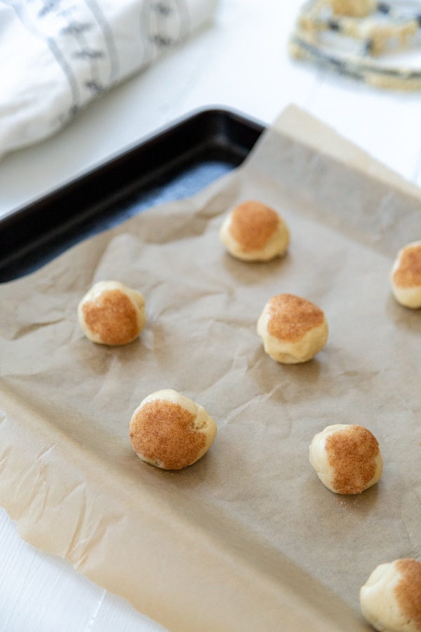 A parchment lined cookie sheet with balls of cookie dough topped with cinnamon sugar.