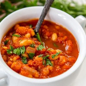 A bowl of tomato and white bean soup with a silver spoon in the bowl.