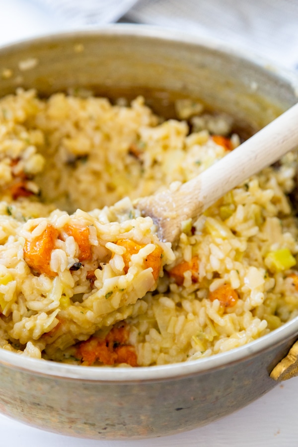 A copper pot with squash risotto and a wooden spoon with risotto on it. 