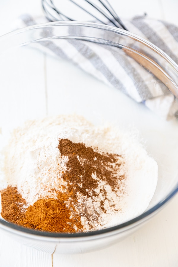 A glass mixing bowl with flour and spices and whisk next to the bowl.