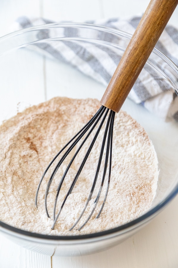 A glass bowl with flour and spices and a whisk.