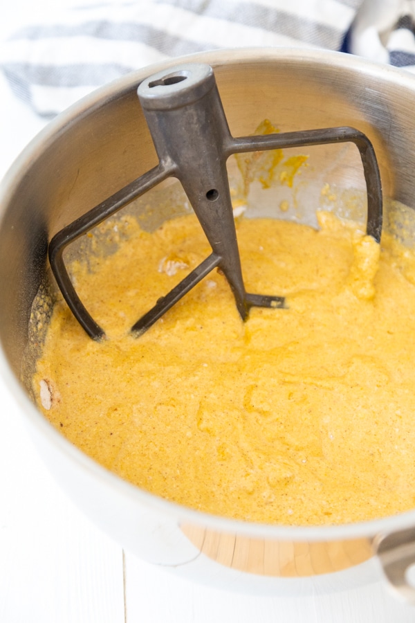 A silver mixing bowl with a mixing paddle and pumpkin bread batter.mi