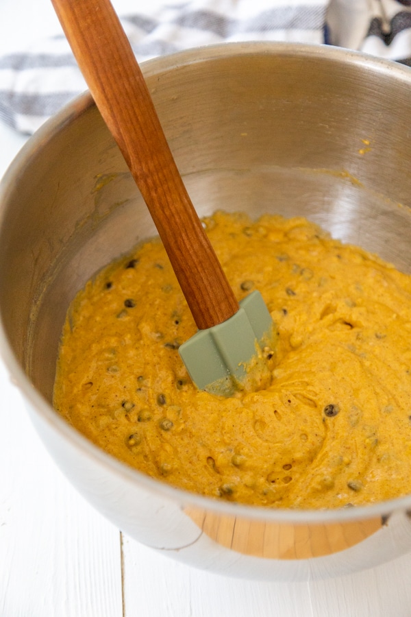 A silver mixing bowl with a spatula stirring chocolate chips into pumpkin bread batter.