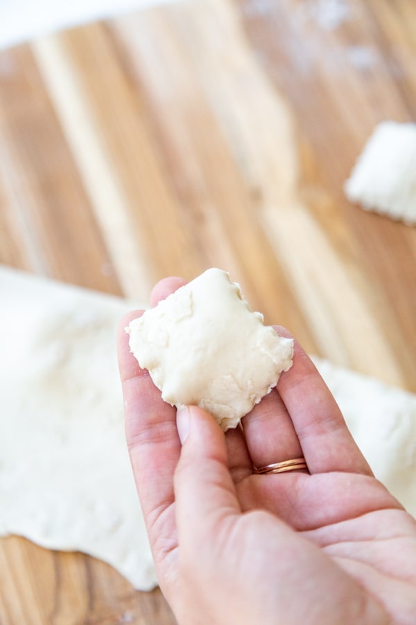 A hand holding a piece of homemade ravioli over a wood board filled with ravioli.