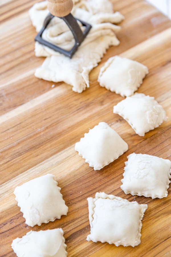 A wood board with homemade ravioli and a ravioli press.