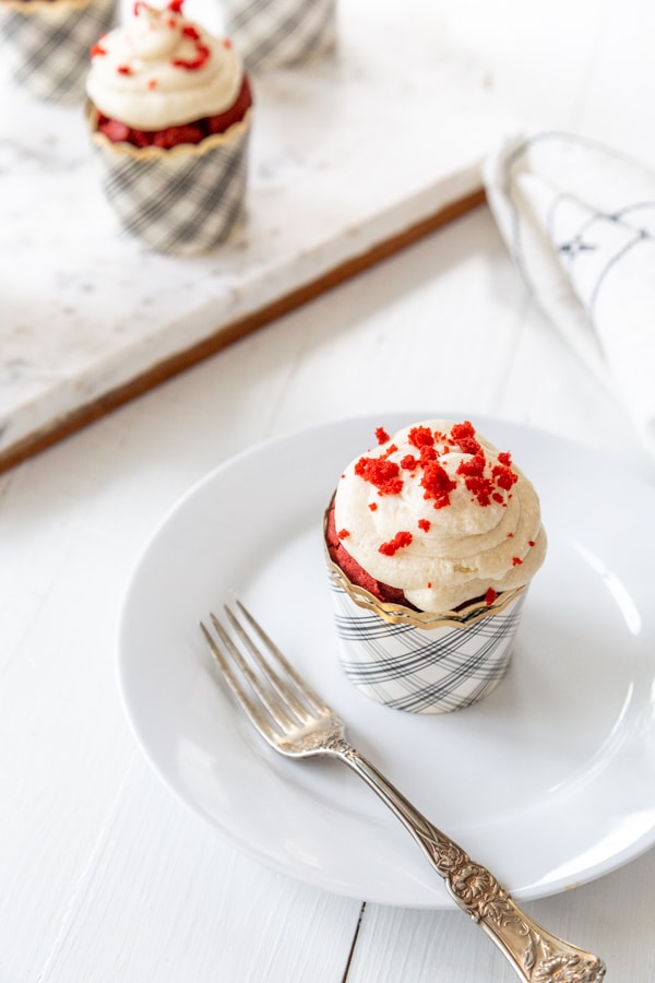 A red velvet cupcake with cream cheese frosting and red cake crumbs sprinkled on top.