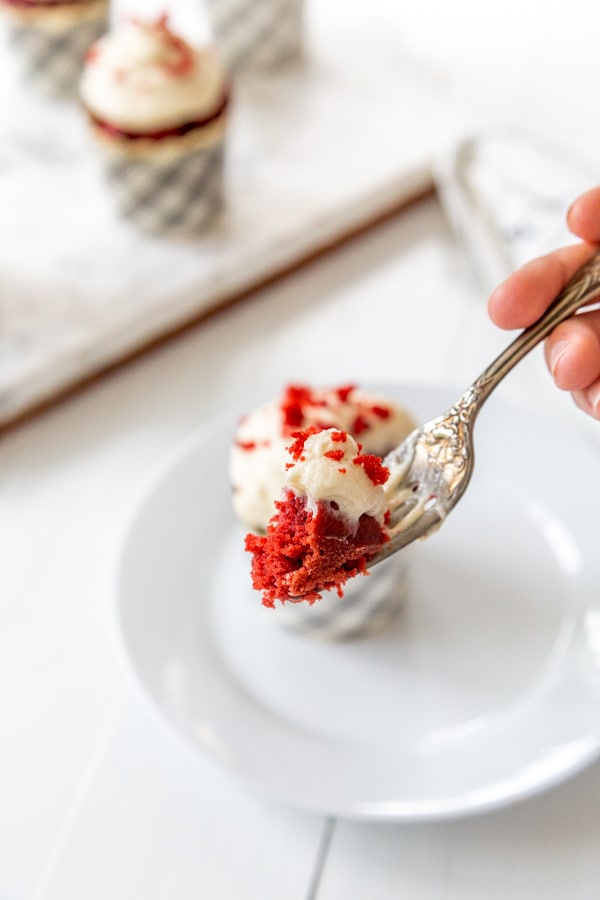 A hand holding a fork with red velvet cake and cream cheese frosting.