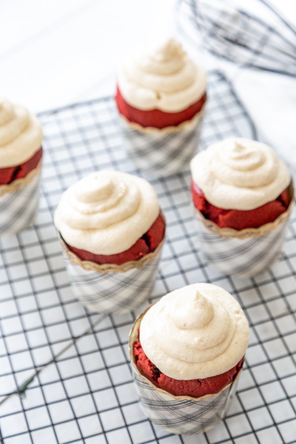 Red velvet cupcakes with piped cream cheese frosting on a wire cooling rack.