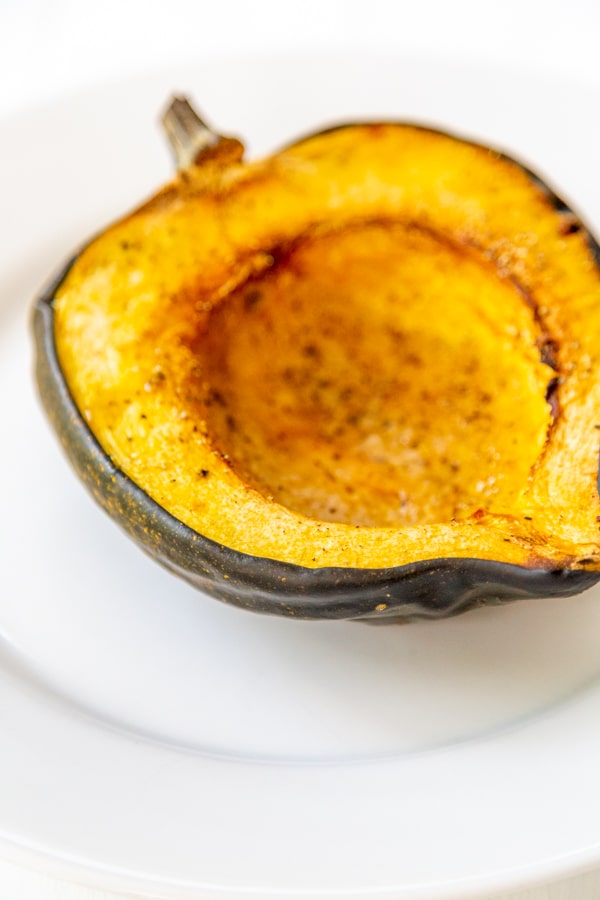 Half of a roasted acorn squash on a white plate. 