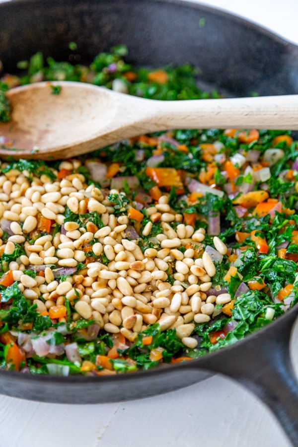 An iron skillet with quinoa, vegetables, and toasted pine nuts.