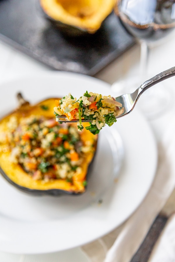 A fork with a serving of stuffed acorn squash and the squash below it on a white plate. 