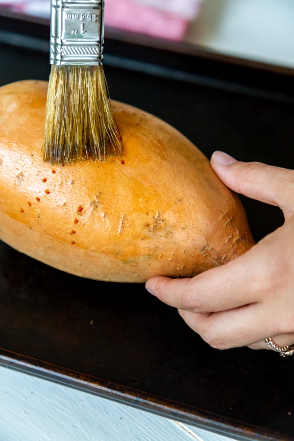 Hands brushing olive oil on a sweet potato.