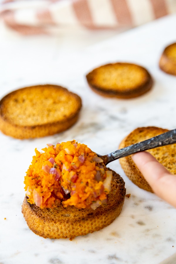 A hand spreading sweet potato dip on toast.
