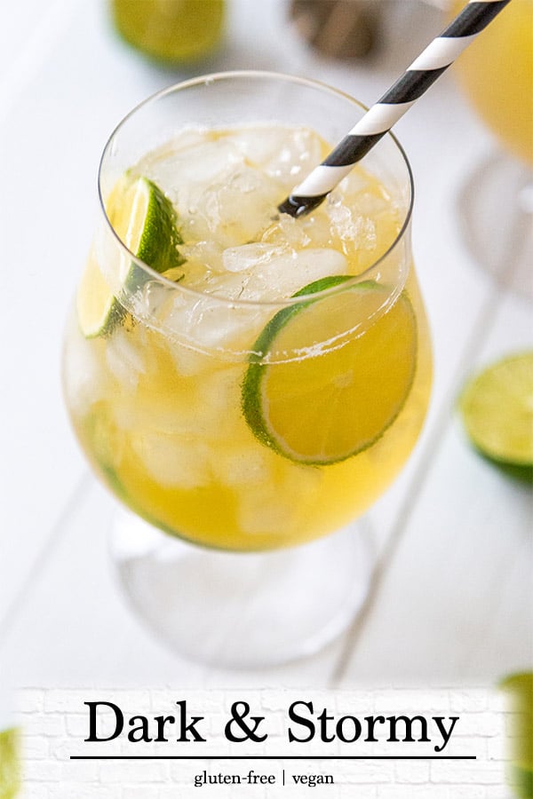 A glass of a dark and stormy cocktail with lime wheels and a black and white straw.