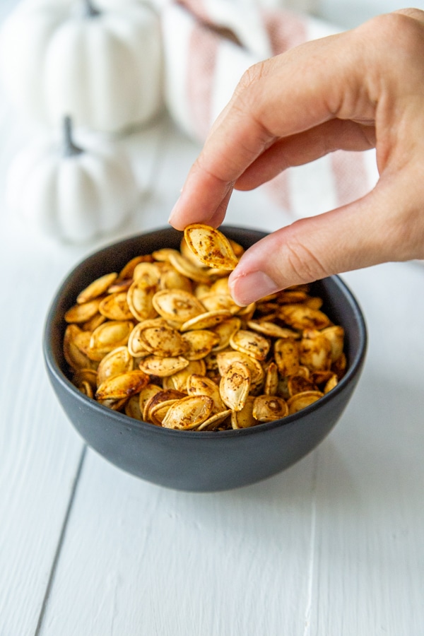 A hand picking up roasted pumpkin seeds from a black bowl.
