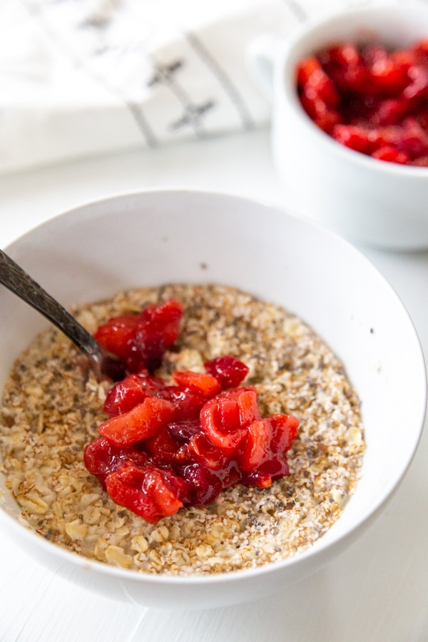 A white bowl with oatmeal and cranberry apple compote. 