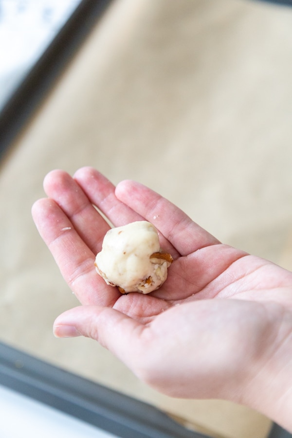 A hand holding a rolled ball of cookie dough over a baking sheet.
