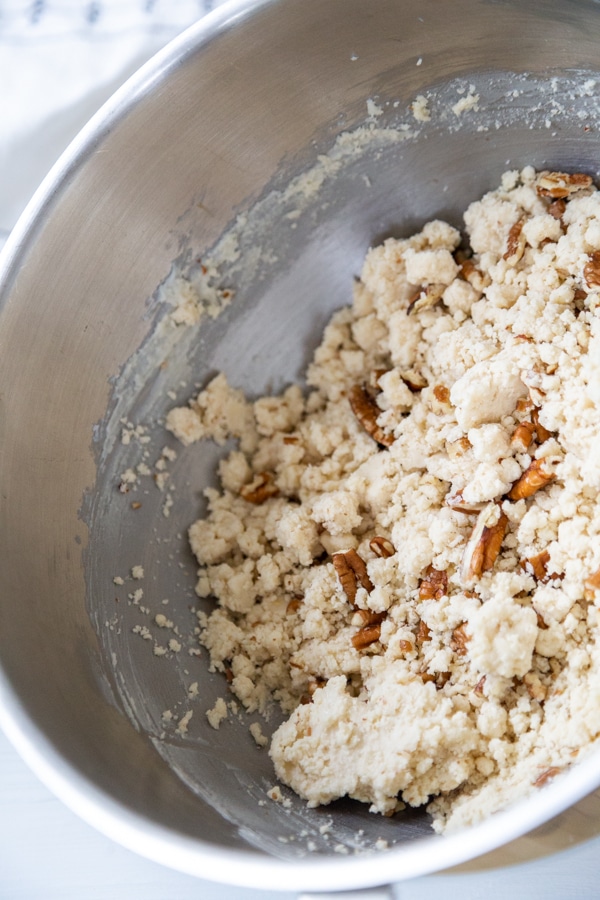 A silver mixing bowl with cookie dough and pecans.
