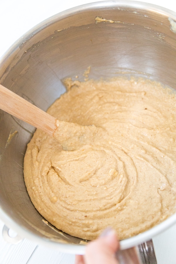 A silver mixing bowl with spice cake batter being stirred with a spatula.