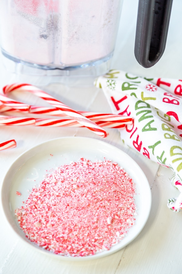 A white plate with ground candy cane and candy canes and a blender next to the plate.