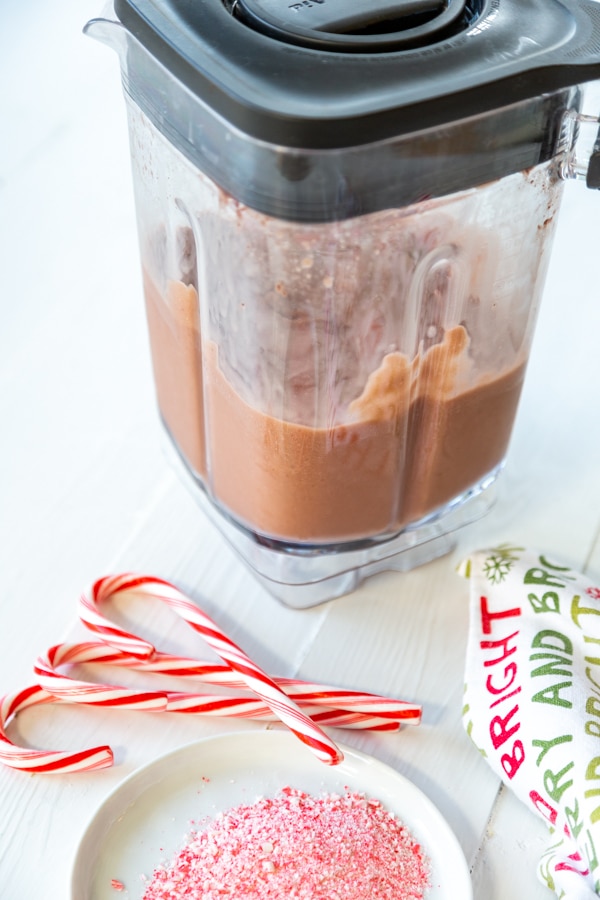 A blender with frozen hot chocolate next to candy canes and a white plate of ground peppermint candy.