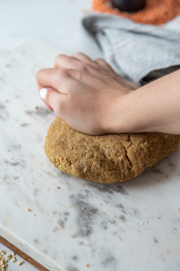 A hand kneading dough on a marble surface.