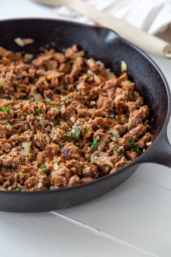 An iron skillet with ground meat and herbs.