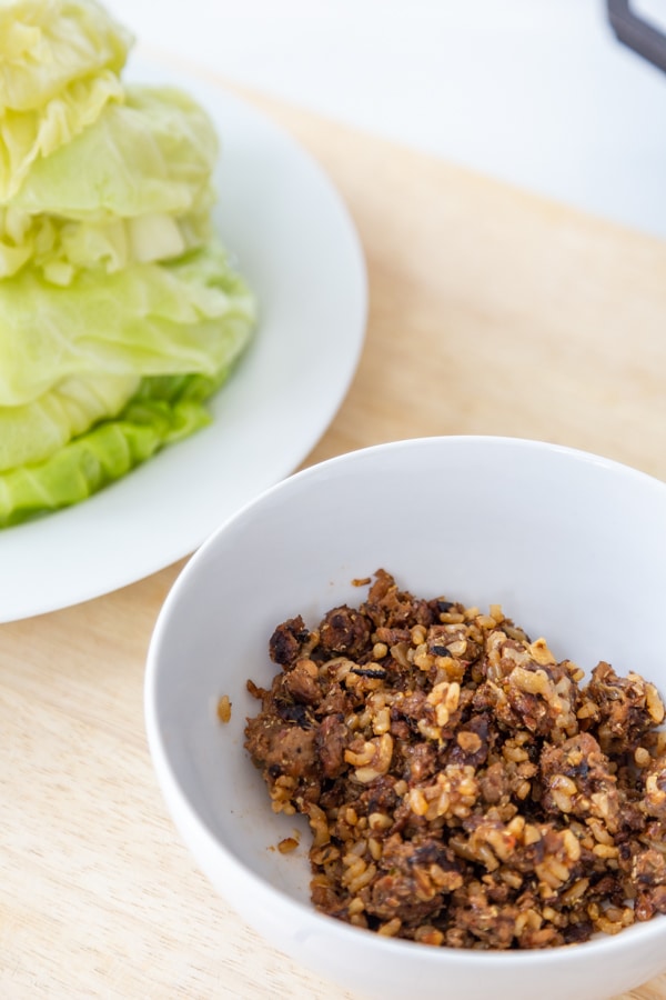 A white bowl with the filling for cabbage rolls and a white plate with cabbage leaves.