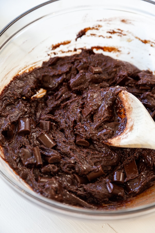 A spoon stirring brownie batter in a glass mixing bowl.