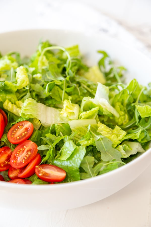 A white bowl with chopped lettuce and sliced cherry tomatoes.