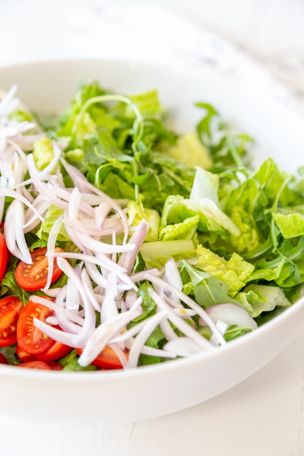 A white bowl with chopped lettuce, sliced tomatoes, and slivered red onion.