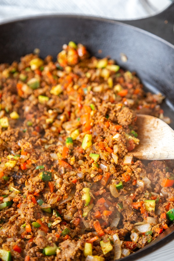 A cast iron skillet with chopped vegetables and chorizo and a wooden spoon. 