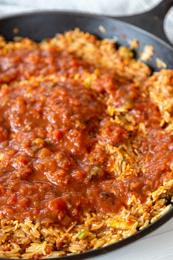 A cast iron skillet with orzo, veggies, and tomatoes.