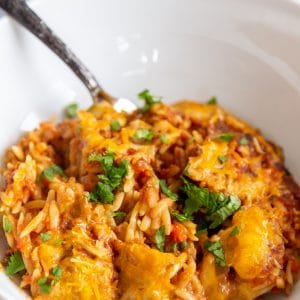 A white bowl with a pasta casserole and silver fork.
