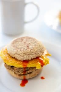 A sausage, egg, and cheese breakfast sandwich with hot sauce dripping down the sandwich.