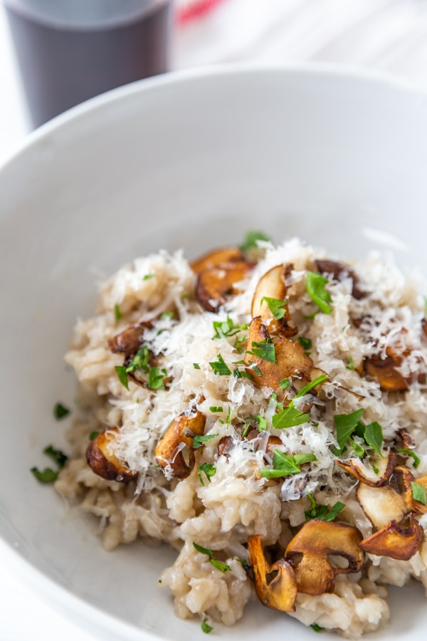 A close up shot of mushroom risotto with chopped basil and grated parmesan cheese on top.