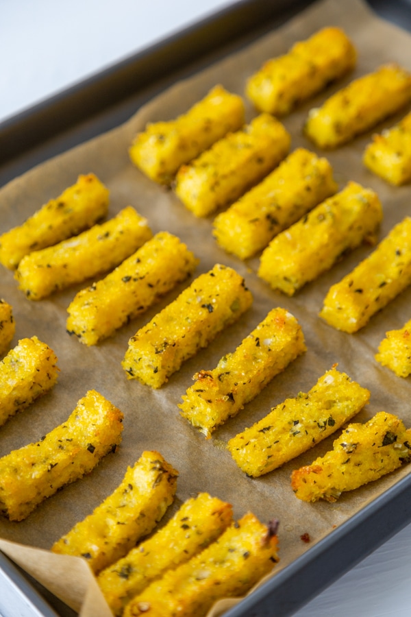 A baking sheet with herbed polenta fries on parchment paper.