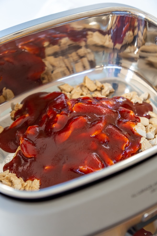 A slow cooker with pulled chicken and BBQ sauce.