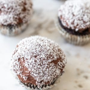 A marble board with 4 chocolate frosted cupcakes with shredded coconut on the tops.