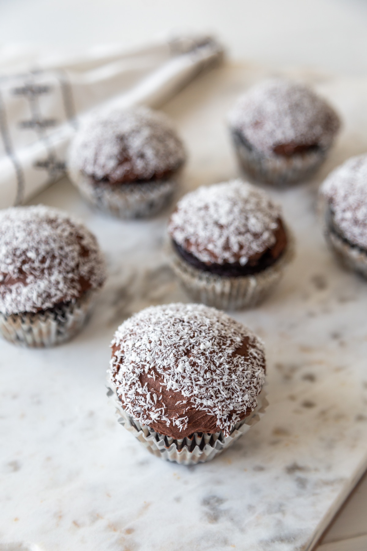 A marble board with 6 chocolate cupcakes with chocolate frosting dipped in shredded coconut.