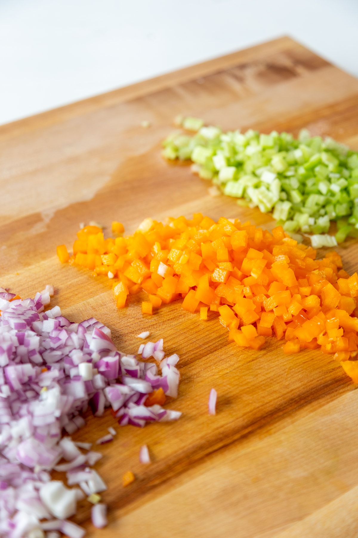 A wood board with finely chopped celery, bell pepper, and red onion.