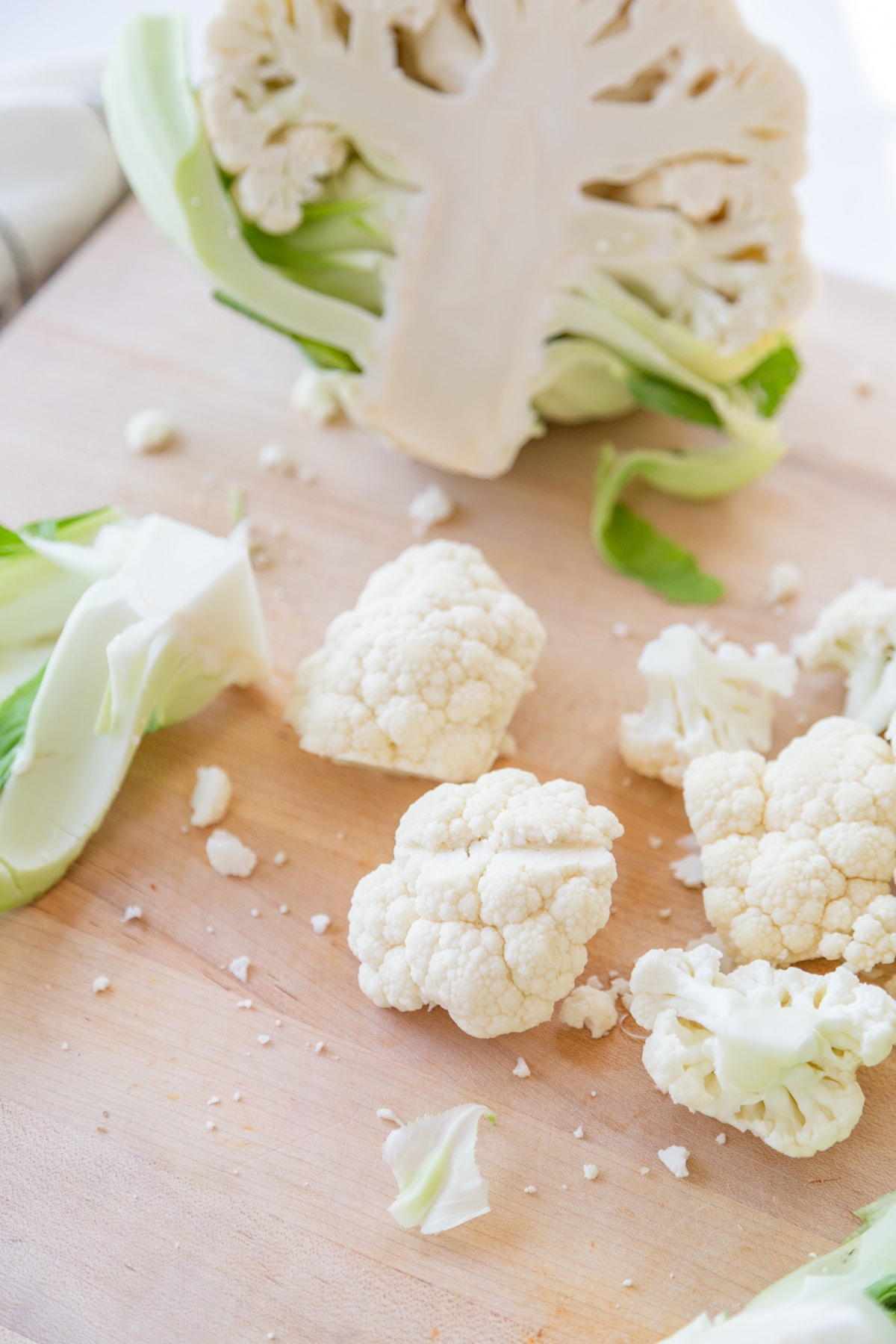 Cauliflower florets and a half of a cauliflower on a wooden cutting board.