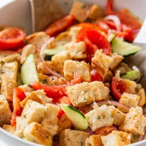 A large white bowl with Panzanella salad and a wood and white serving spoon tossing the salad.